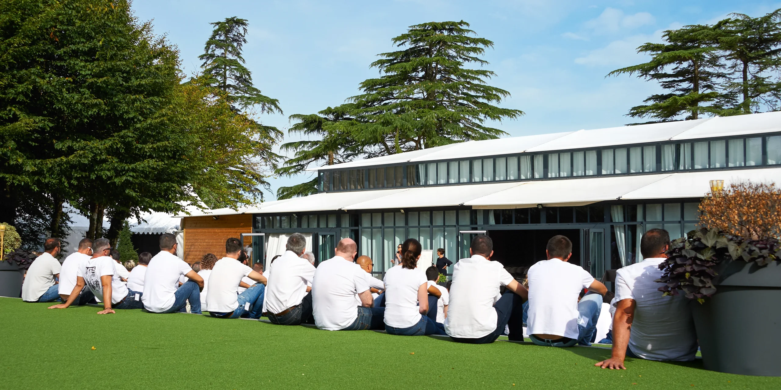 Groupe assis sur pelouse devant bâtiment moderne