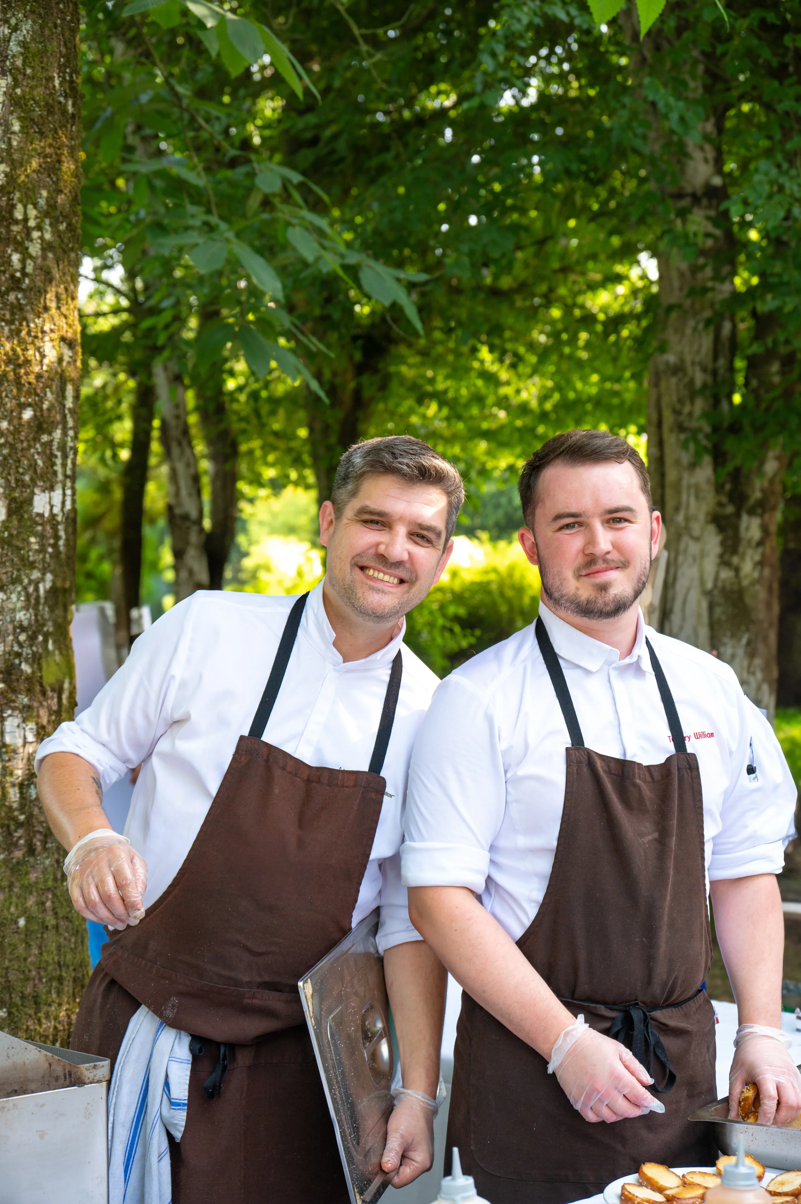 Deux chefs souriants en extérieur préparant des plats