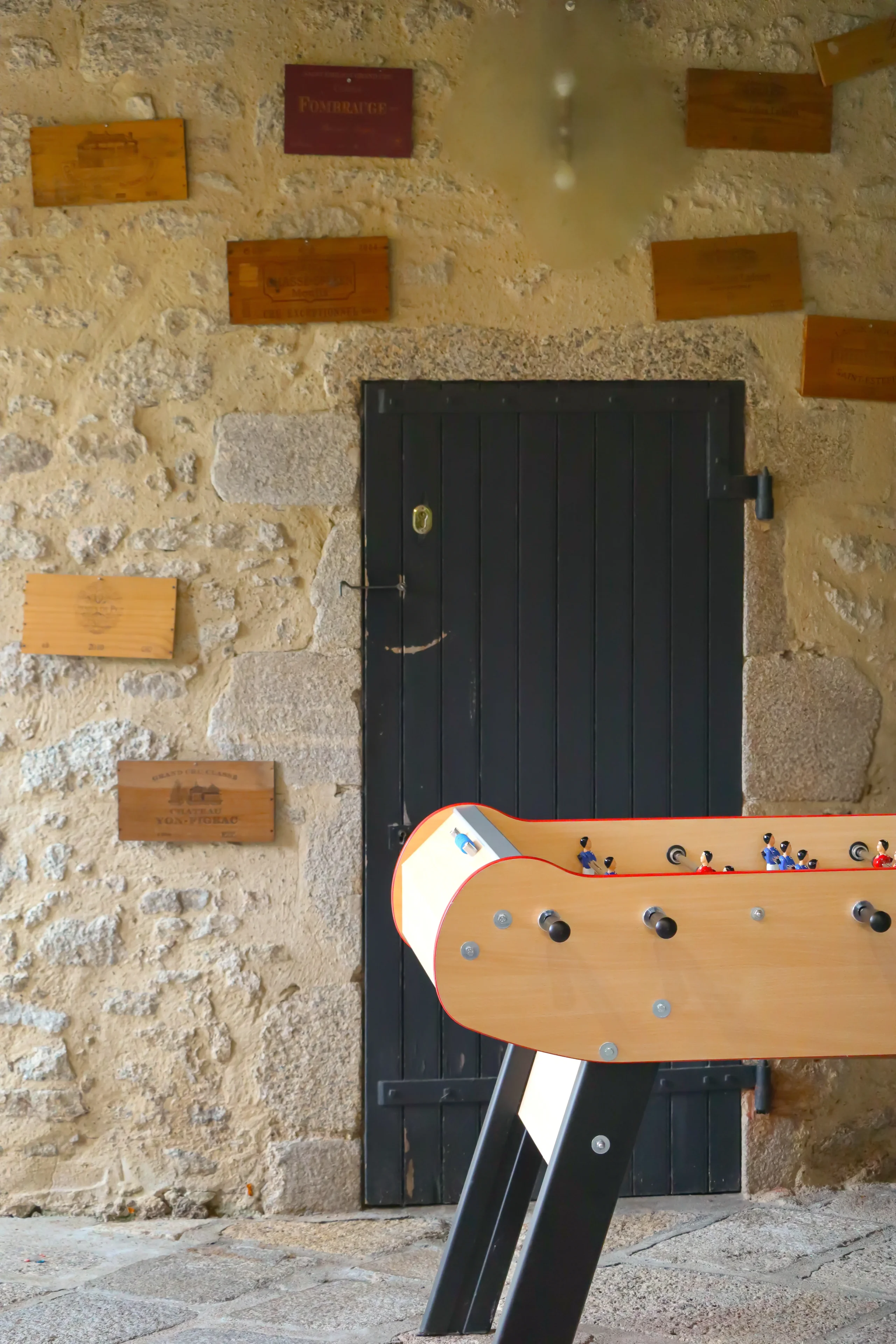 Baby-foot devant porte noire et mur en pierre