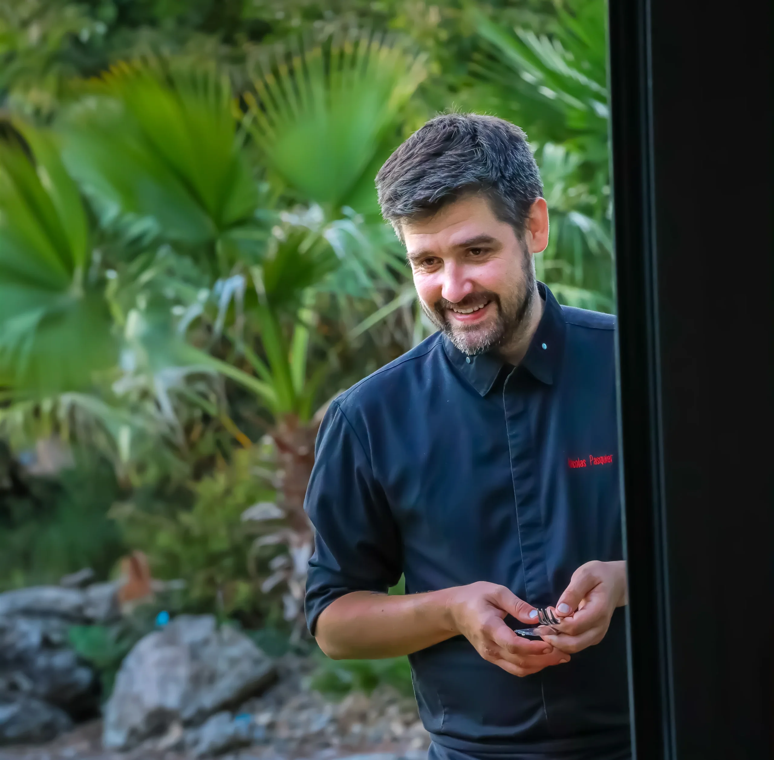 Chef souriant en veste noire dans un jardin