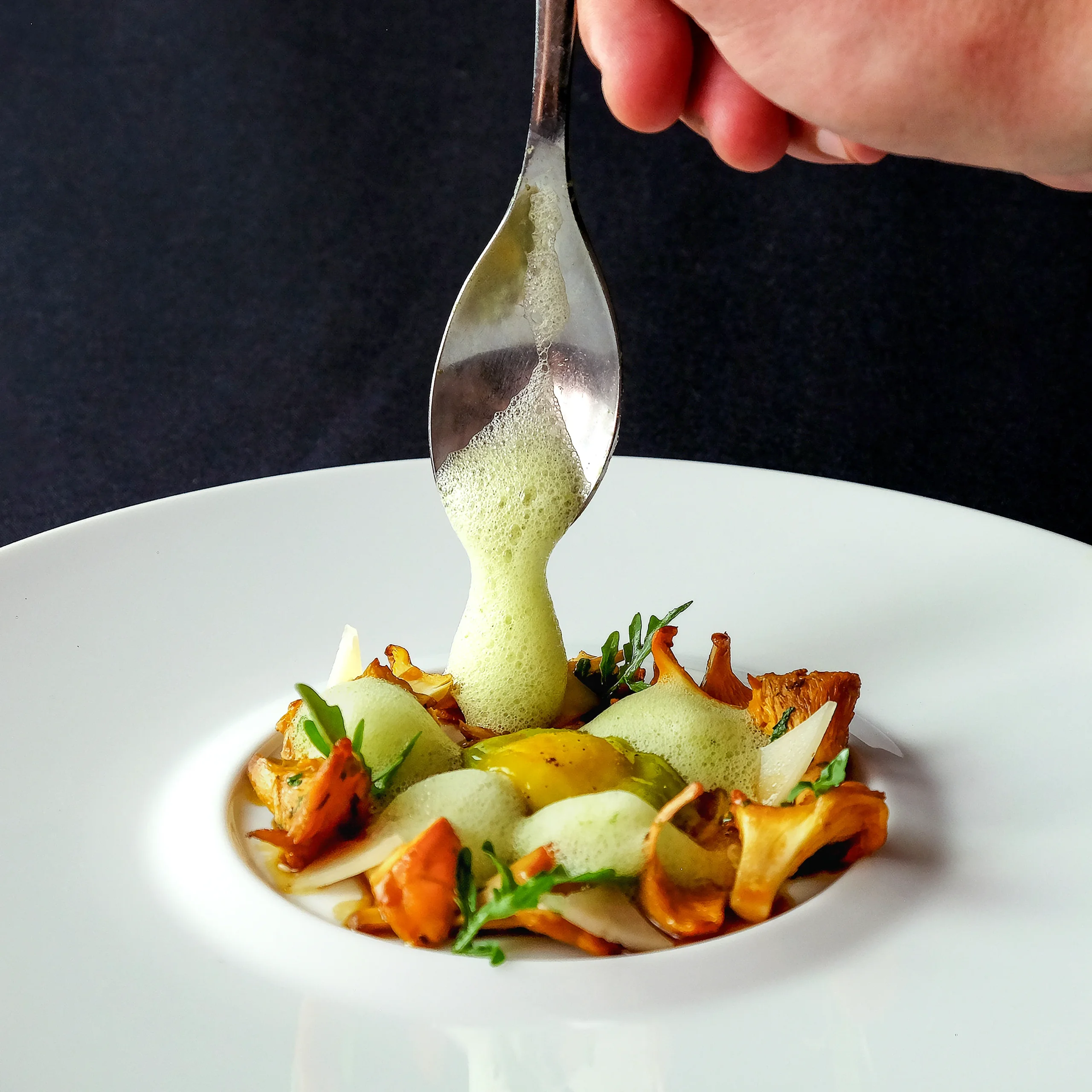 Émulsion verte versée sur plat gastronomique aux girolles